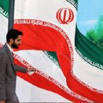 رجل يسير في طهران بجوار جدارية رسم عليها علم الجمهورية الإسلامية في إيران