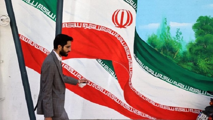 رجل يسير في طهران بجوار جدارية رسم عليها علم الجمهورية الإسلامية في إيران